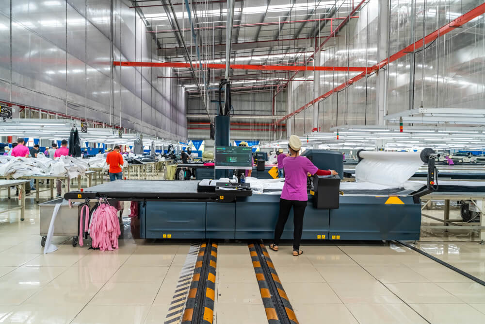 Indian employees working in garment manufacturing factory operating fabric-cutting machinery